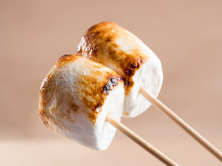 Two sweet marshmallows with baked crust on a brown background.