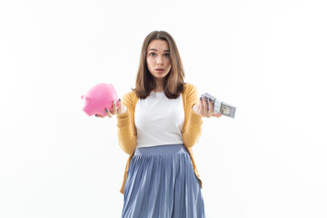 A beautiful brunette holds a pink piggy bank in one hand and a wad of money in the other. Concept of depositing money in a bank