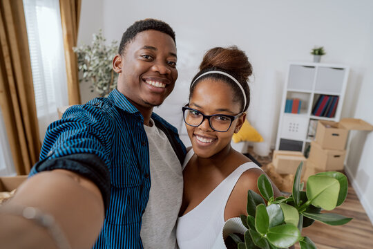 A couple in love moves into their first apartment, they take a picture together with phone on social media after moving in, smiling, happy, bragging about new home, boxes in background