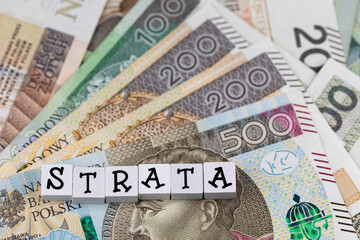 The wording "Strata" translated as "Loss" plus many Polish banknotes. Increasing costs of business activity. Photo taken under artificial, soft light
