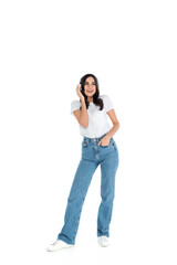 full length view of happy woman in jeans listening music in headphones on white.