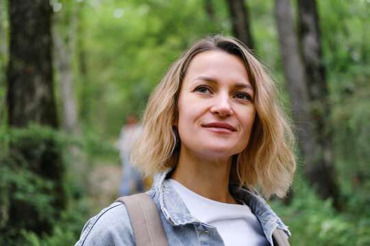 A young Caucasian woman walks along a forest mountain road. Casual blue denim clothes and backpack. Travel, healthy lifestyle and freedom.