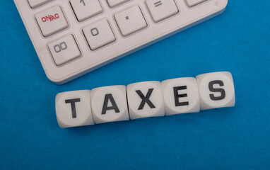 Taxes word block closeup view with calculator in background