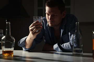 Addicted man with alcoholic drink at table in kitchen