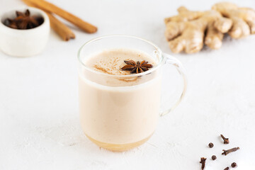Masala tea with milk, ginger root and spices in a glass mug on the table. Lactose free, vegan.