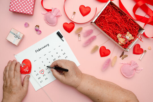 Flat lay on a pink table on which an elderly woman is preparing for the celebration of Valentine's Day marks the date February 14 on the calendar, placed hearts and various paraphernalia on the table.