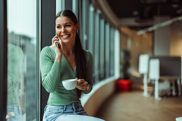 Relaxed caucasian manager, looking through a window with a cup in her hands.