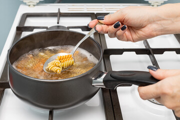 a woman's hand takes a spoonful of pasta out of the pan