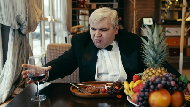 Fat ugly man eats steak in a restaurant with wine.