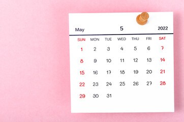 May 2022 calencar and wooden push pin on pink background.