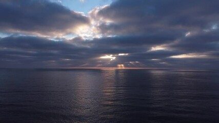 Drone view of sun rays peaking through thick dark clouds over the ocean in the evening. can be used for cinematography, establishing shot or in a motivational video.