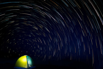 Adventurer's tent at night and the backdrop of Star trails against black night sky