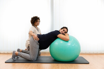 A pregnant woman doing breathing exercises and resting on a fitness ball with the help of her...