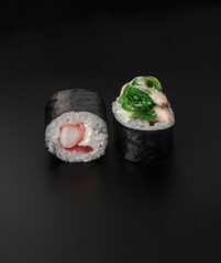 maki sushi with shrimp and chuka seaweed on black background closeup