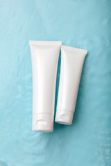 White cosmetic products in tubes on color blue background with drops. Mock up skincare cosmetic packages on water surface. Natural moisturizing water balance cosmetics beauty product.