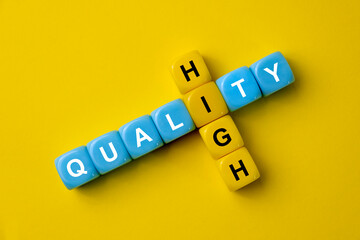 Words HIGH QUALITY on plastic colorful cubes on yellow background. Evaluation of good or services business concept. Concept of TQM, Total Quality Management or improvement.