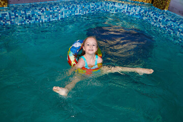 Nice child swiming in blue small pool. Girl have fun in water indoors