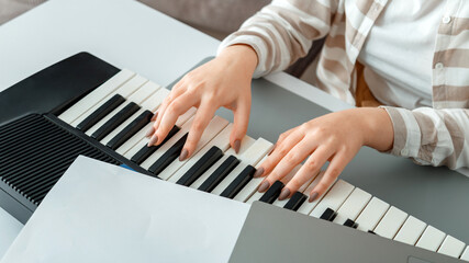 Fototapeta na wymiar Woman playing piano record music on synthesizer using notes and laptop. Female hands musician pianist improves skills playing piano. Online Music education hobby vocals singing. Long web banner.