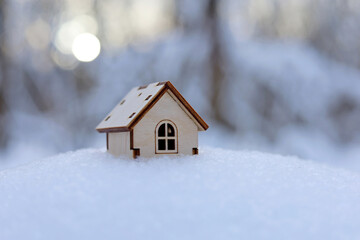 Wooden house model in a snow on winter forest background. Concept of country cottage, real estate in ecologically clean area