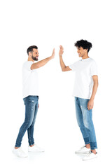 full length view of interracial friends in jeans and t-shirts giving high five on white.
