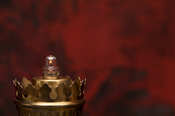 Close-up of an oil lamp with a glowing bulb mounted. In the background an abstract black and red background.