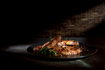 Steak with sauce on a black plate. Meat with spices and rosemary on a dark background. Contrasting light as an artistic effect. Copy space and free space for text near food.