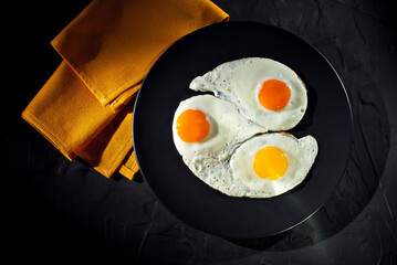 Scrambled eggs in a black plate. Fried eggs on an old concrete table. Yellow tablecloth near the plate.