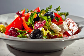 Salad with tomatoes, peppers, olives, cheese and cabbage. Fresh salad in a white plate on a light background.