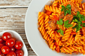 Pasta with meat and tomatoes in a white plate. Pasta on a shabby wooden table.