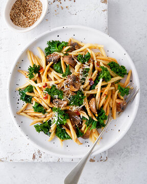 Whole grain pasta with kale, mushrooms, parmezan cheese in white plate on light background.
