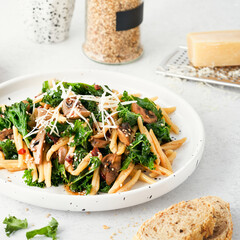 Whole grain pasta with kale, mushrooms, parmezan cheese in white plate on light background.