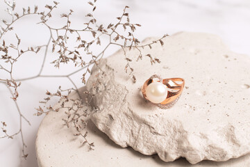 Gold ring with pearl on stone podium with dry flowers