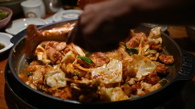 Chef using wooden flipper stir-fried a Dakgalbi barbeque chicken with vegetable on hot pan