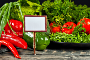 Various vegetables in a pile on a black background. A place to advertise products. Copy space and place for text near greenery. Wooden sign and price tag in vegetables.