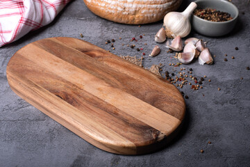 Wooden cutting board, spices, garlic, bread on dark stone countertop, background. Culinary concept, composition.