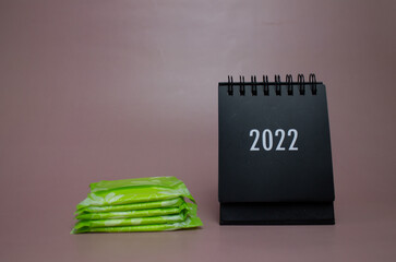 women's sanitary pads in green packaging, black desktop calendar, pink background
