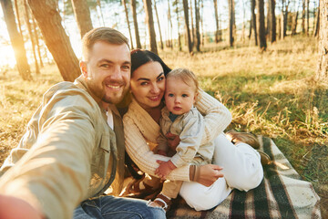 Making a selfie. Happy family of father, mother and little daughter is in the forest