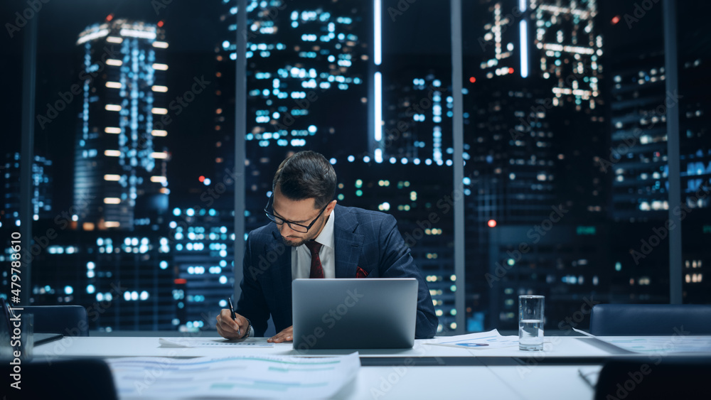 Poster successful handsome businessman working on laptop computer in big city office late in the evening. f