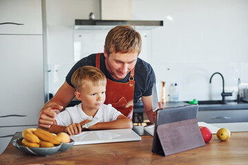 Learning how to cook. Father and son is indoors at home together