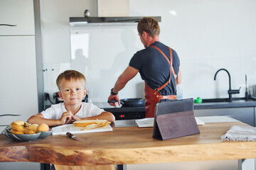Learning how to cook. Father and son is indoors at home together