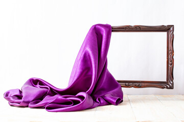 Purple satin fabric unveiling a levitating wooden empty frame, on white background
