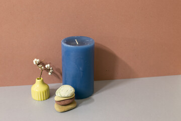 Navy candle and stack of pebble stones and dry plant on gray table. brown wall background. home decor interior