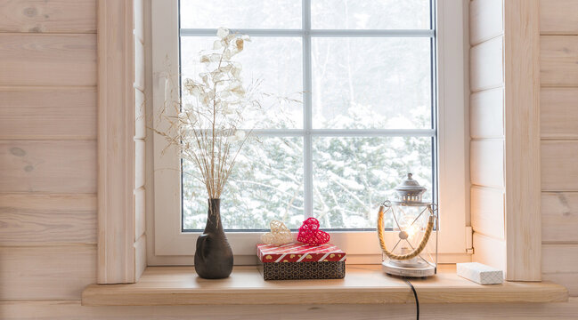 Romantic window in a white wooden house overlooking the winter garden, Scandinavian style. Lantern, candles and heart on the windowsill.