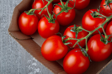 Cherry tomatoes in a cardboard box on a wooden background. Fresh tomatoes with copy space