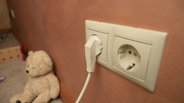 Young woman inserts the plug of the electrical appliance into the socket in the children's room. Close-up of a power outlet that accepts and exits an electrical appliance plug