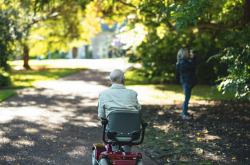 Senior walks through the park. Elderly person with a locomotive disability is riding in a motorized chair through the park