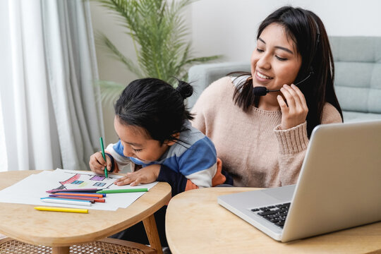 Happy asian mother working on computer at home with her child - Busy family mom giving call center support - Focus on kid right hand