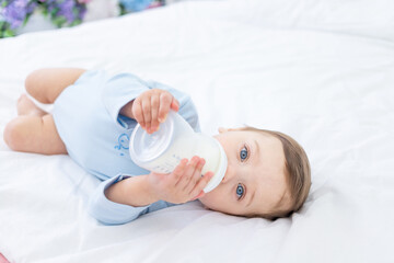 Obraz na płótnie Canvas baby boy with a bottle of milk on the bed for sleeping in a blue bodysuit, baby food concept
