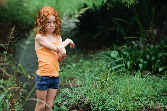 Young redhead girl standing in bushland holding her arm