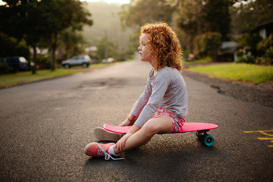 Young girl sitting on a skateboard on a road